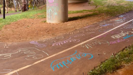 Example: Eternity repeatedly written in chalk on walkway. Colurful pillar in background.