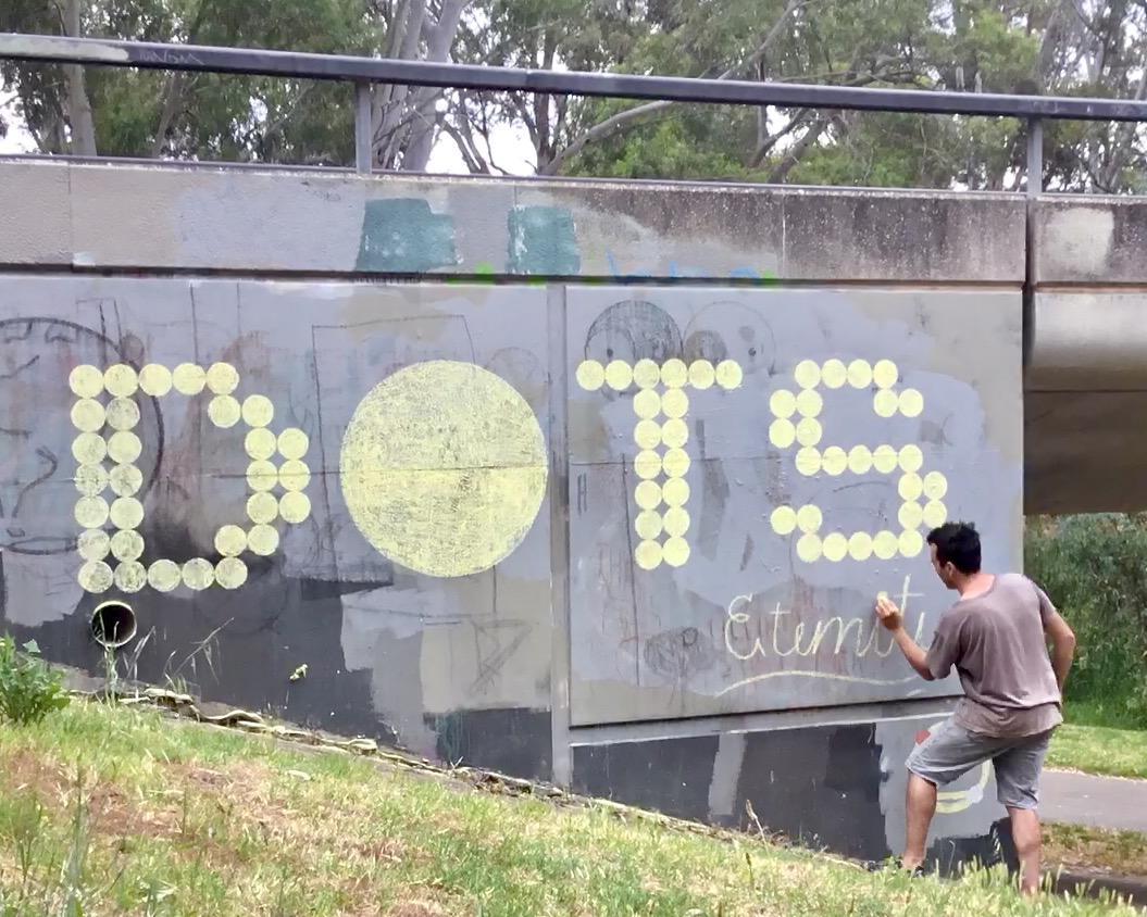 Man chalking the words 'DOTS' and "eternity' on wall