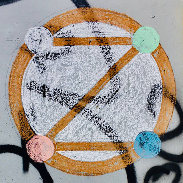 geometric dotZero symbol in chalk on wall with graffiti behind