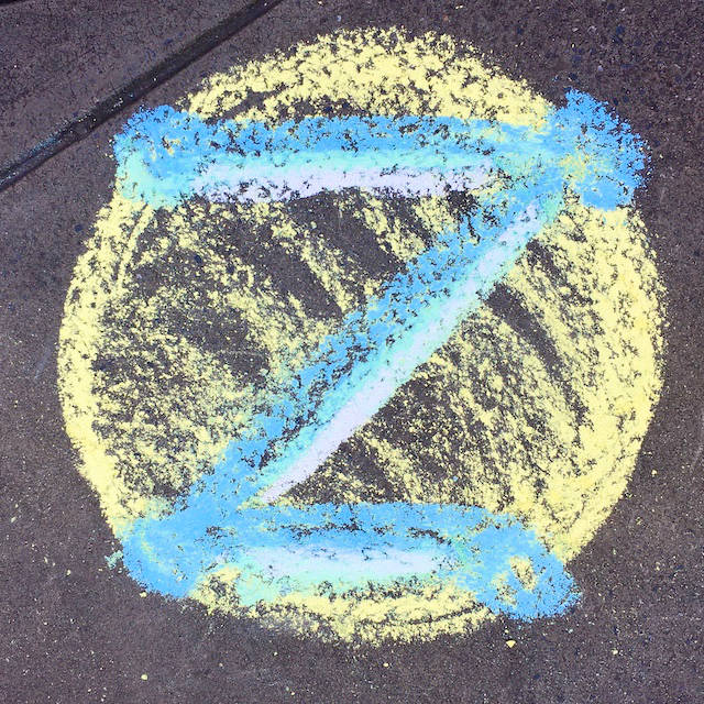 Blue and white dotZero symbol in chalk on pavement. Yellow background.
