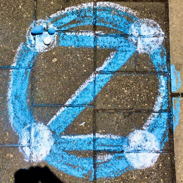 Blue dotZero symbol in chalk, on square pavers. Stubs of pavement chalk.