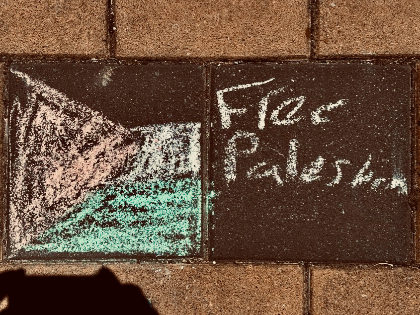 Roughly drawn Palestinian flag in pavement chalk with 'free Palestine' scrawled alongside.