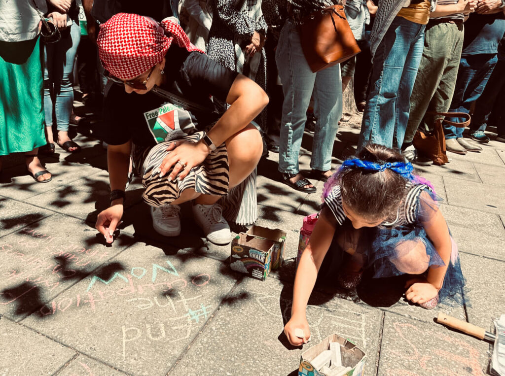 Woman, wearing 'free Palestine' t-shirt chalking #EndTheOccupationNow with pavement chalk